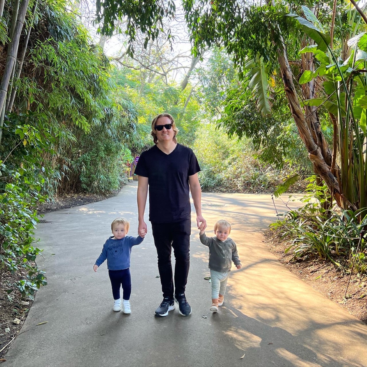 isaac walking along a path holding the hands of his twin toddler boys